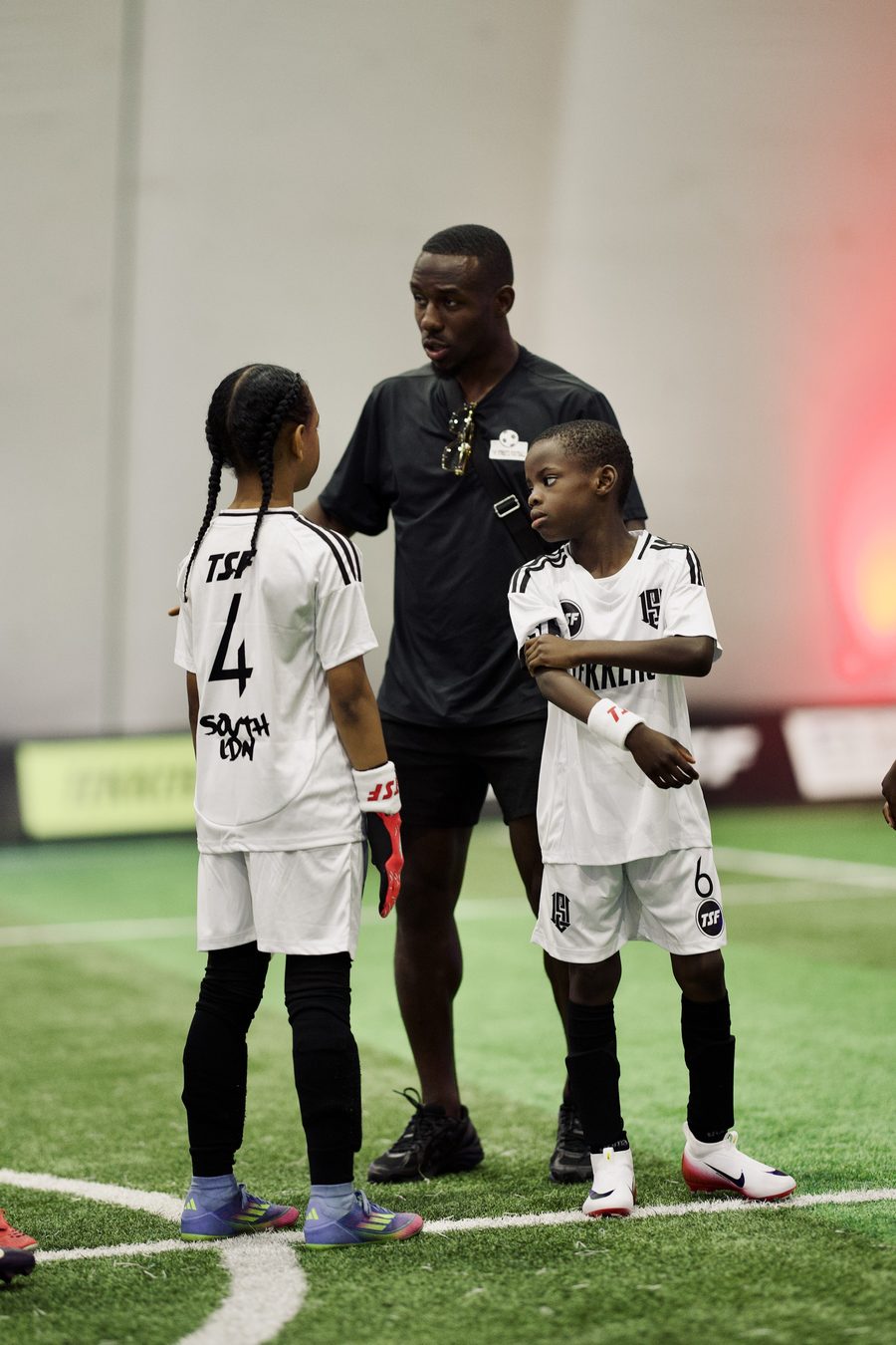 A Tekkers coach with two young players in Tekkers kit on an indoor pitch