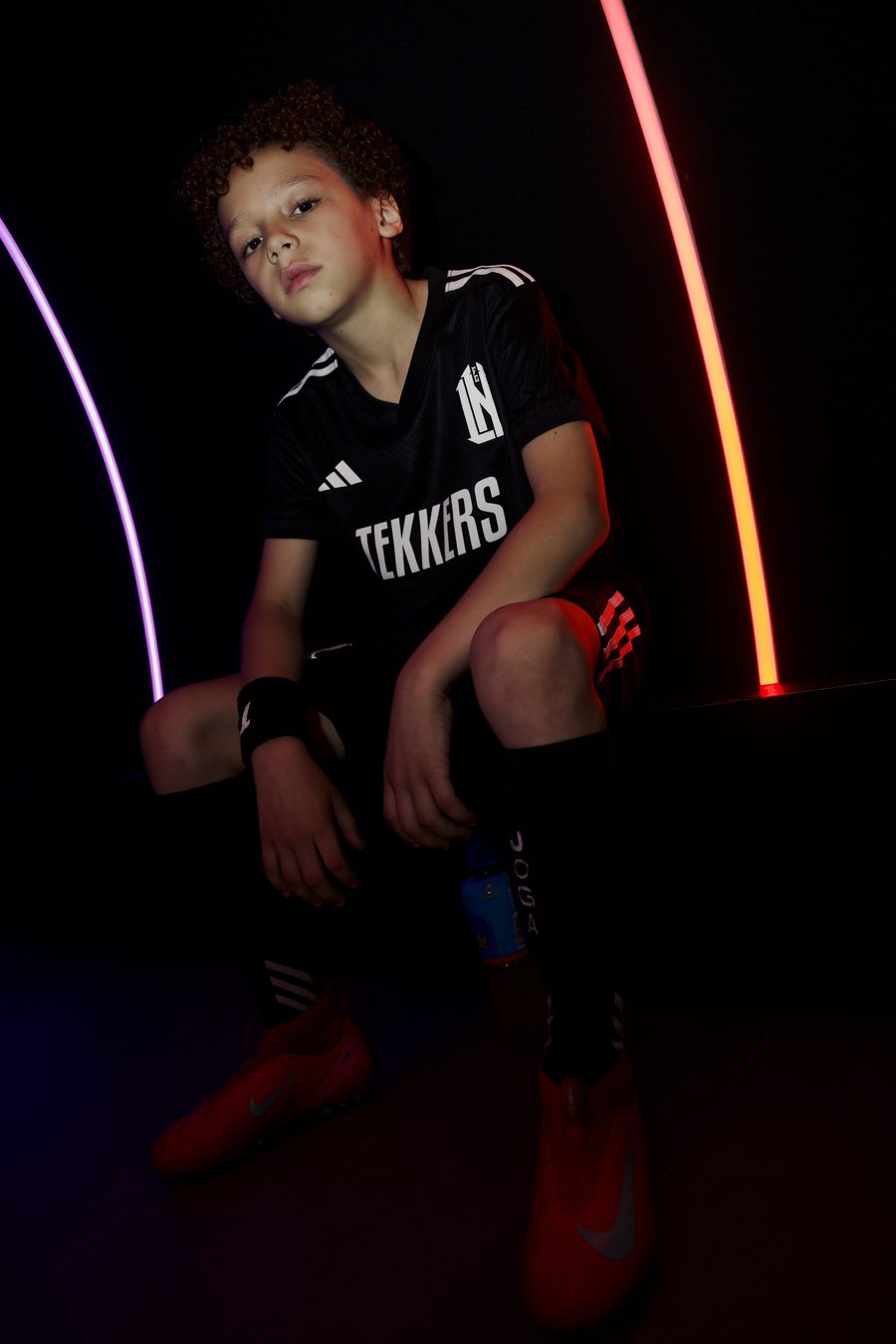 A young player in a black Tekkers shirt sitting alone under neon lights