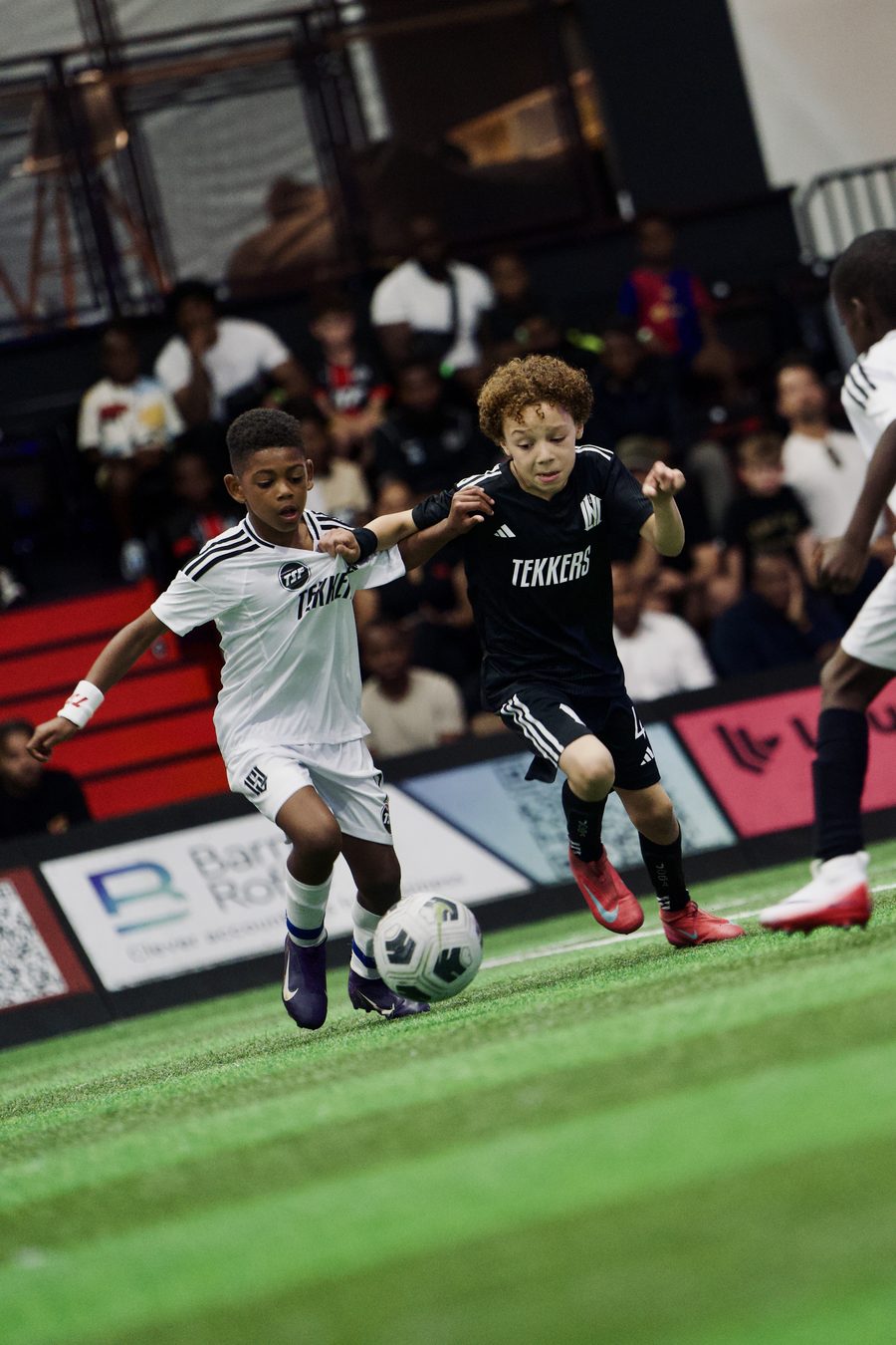 Two young players in Tekkers kit battling for the ball at an indoor venue